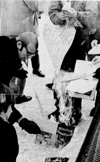 A student sets fire to a student handbook in protest.