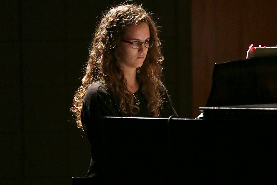 A person wearing a black shirt plays a black piano.