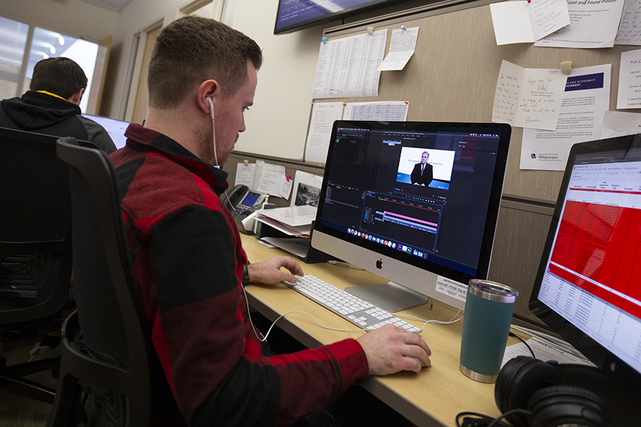 A student wears headphones while working on a Mac computer.