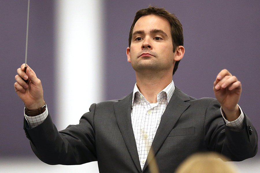 A person wearing a suit jacket raises their hands to conduct.