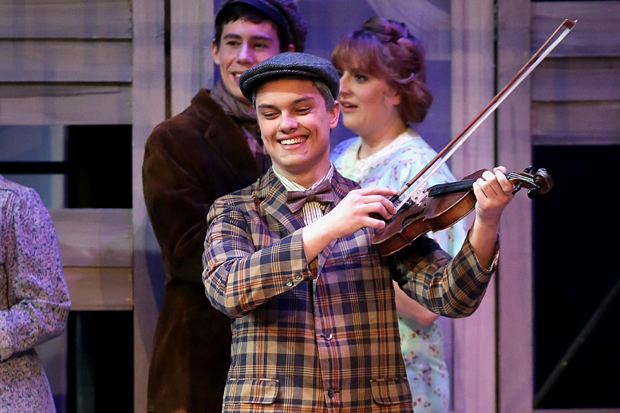 A student plays the violin on stage during a theatre performance.