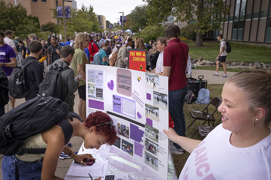 A student signs up at a table with a sign that says UWW dance company during the involvement fair.