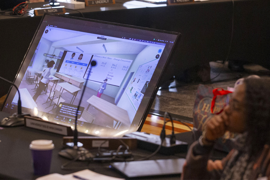 A person sits next to a screen monitor showing a classroom created by artificial intelligence.