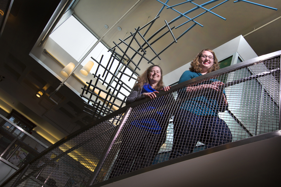 Two students stand on a staircase, smiling at the camera.