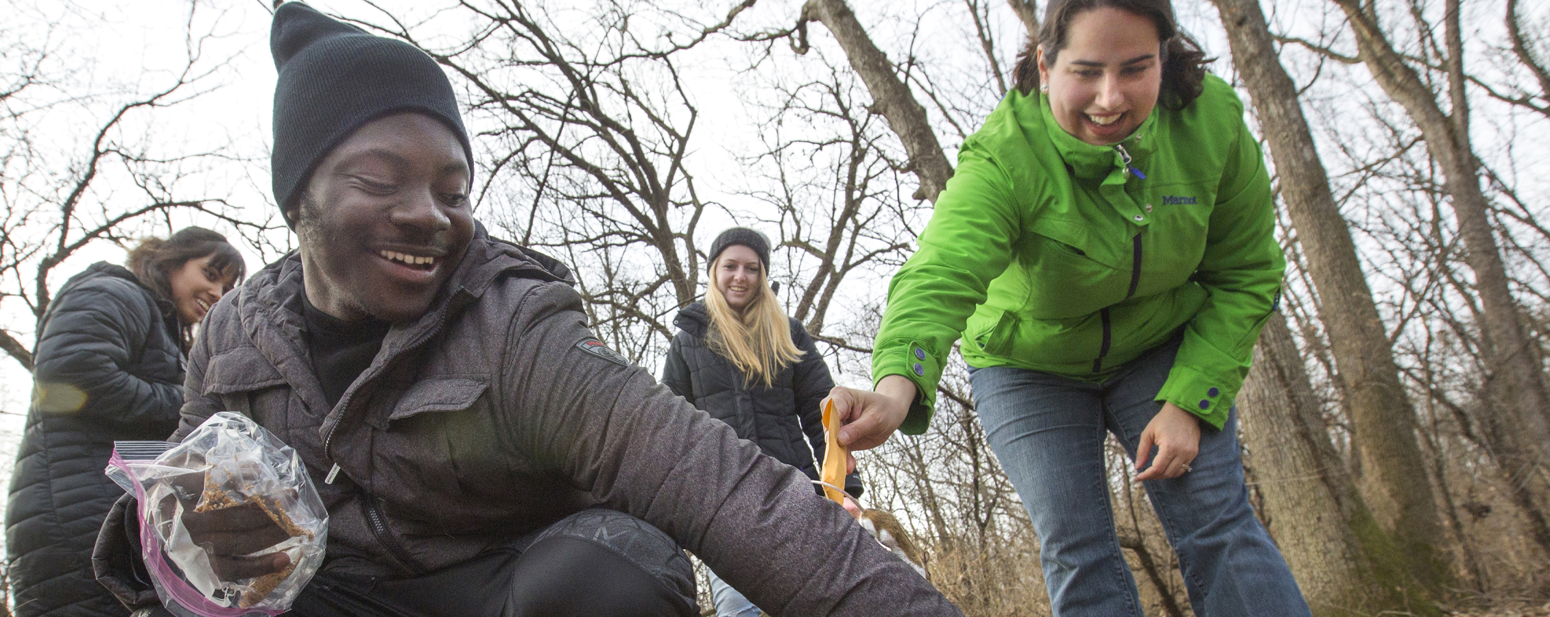 A student holds out their arm as a mouse runs up while they're in the woods for class.