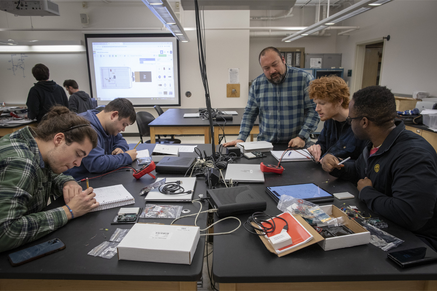 Students work with a faculty member as they build circuitry at a large table.