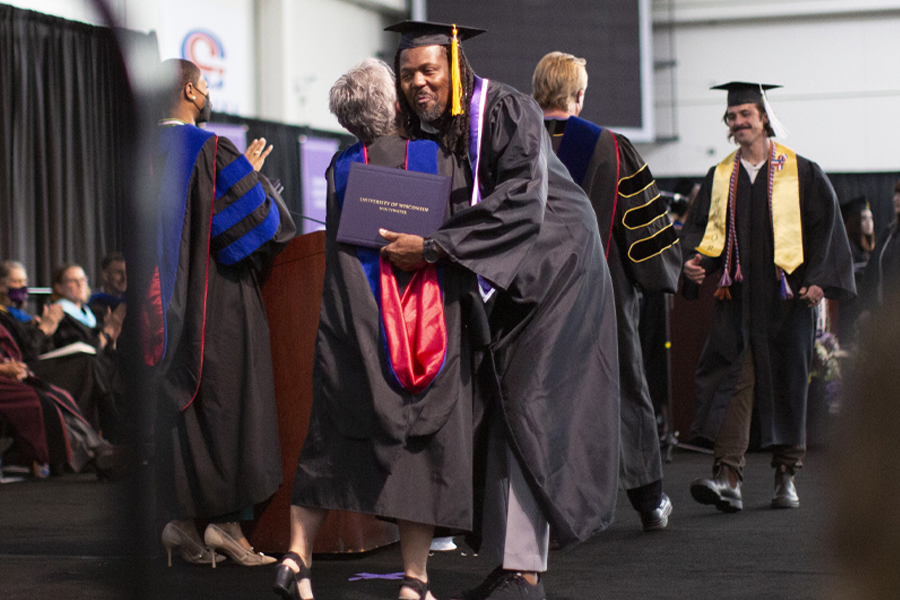 A student crosses the stage in cap and gown.