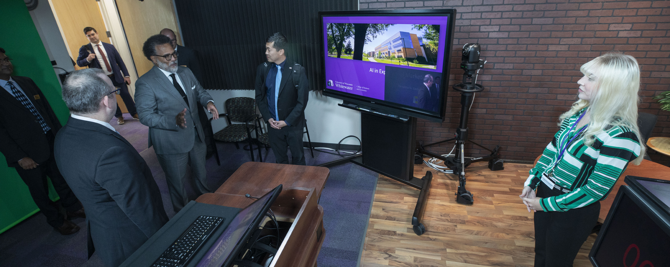 A group of people tour a technology room in Hyland Hall with a green screen and computer screens.