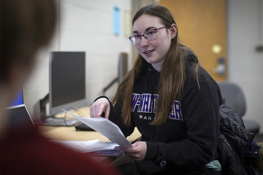 A student holds a book while working on a laptop.