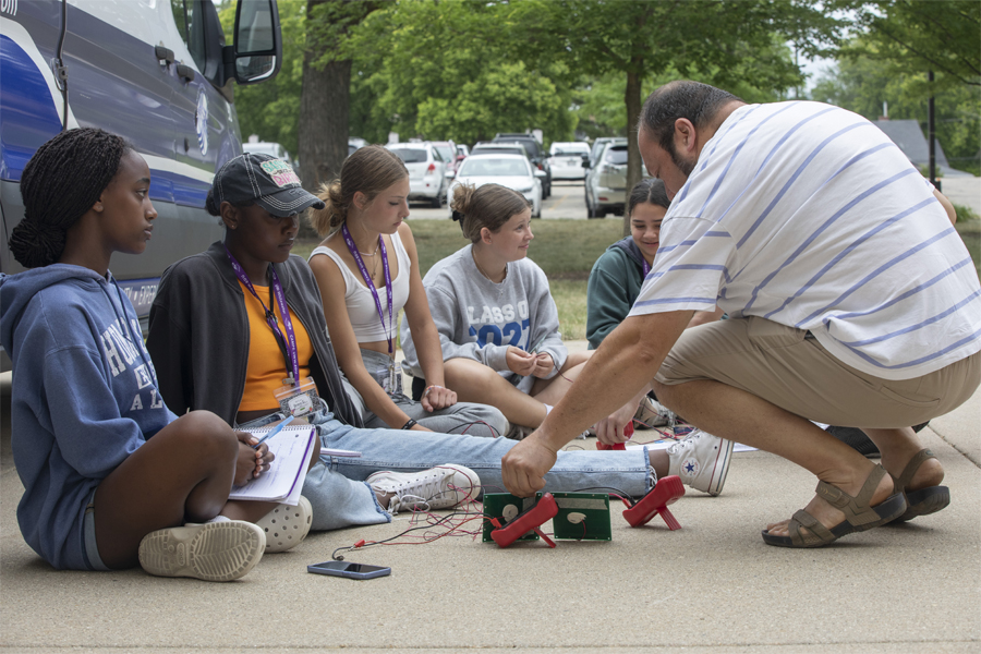 A faculty member sits with students outdoors.