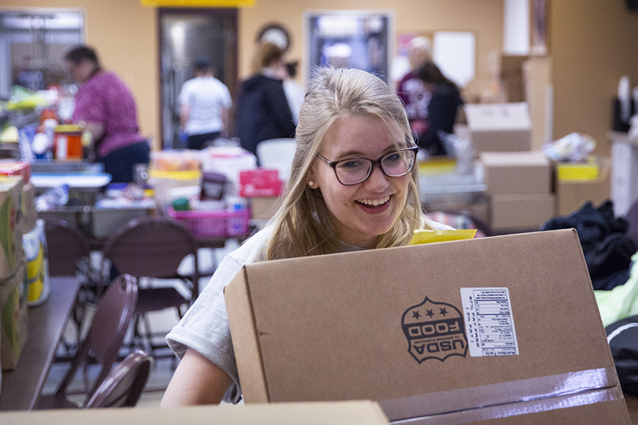 A student smiles while carrying a cardboard box.