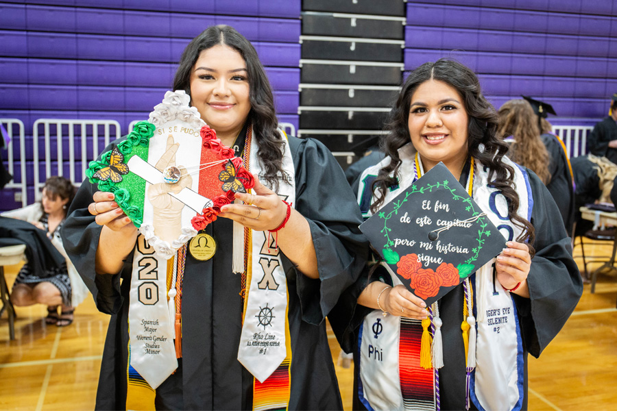 Two students holding up their decorated caps at commencement.