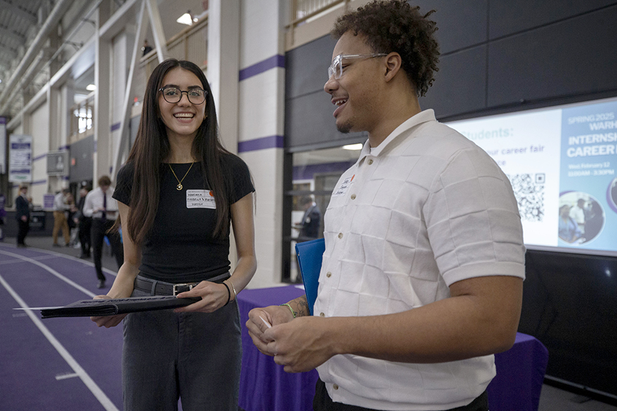 Two people stand together and smile in the fieldhouse during a career fair.