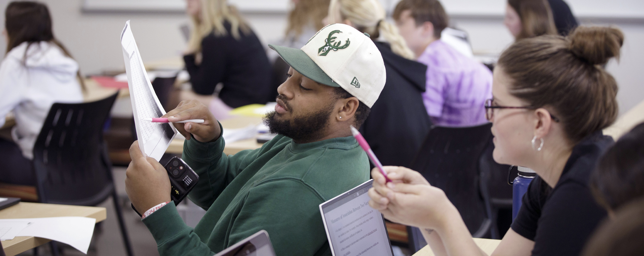 A student leans back in their chair to discuss something on a paper with the student sitting behind them.