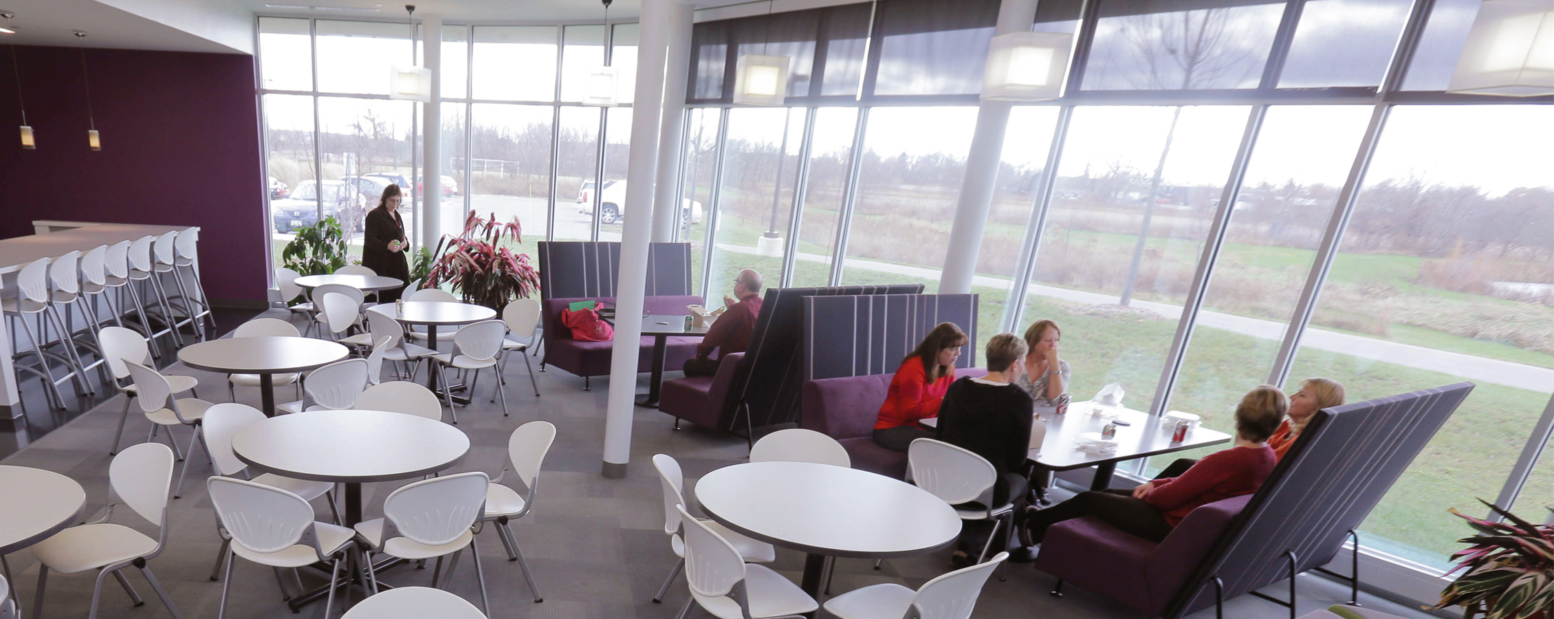 People sit in a room with large windows and white tables and chairs.