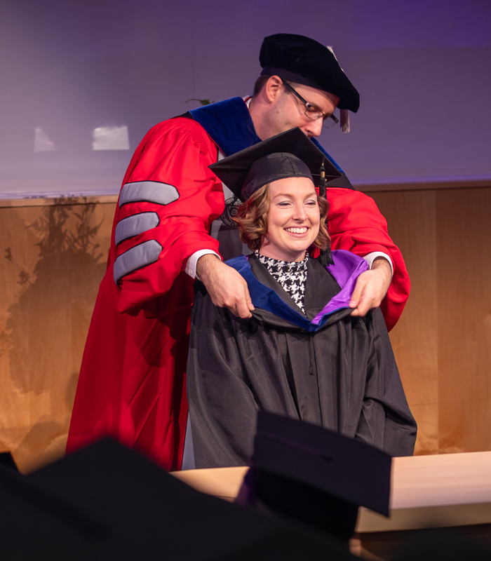 A person smiles as they receive their hood during a graduation ceremony.