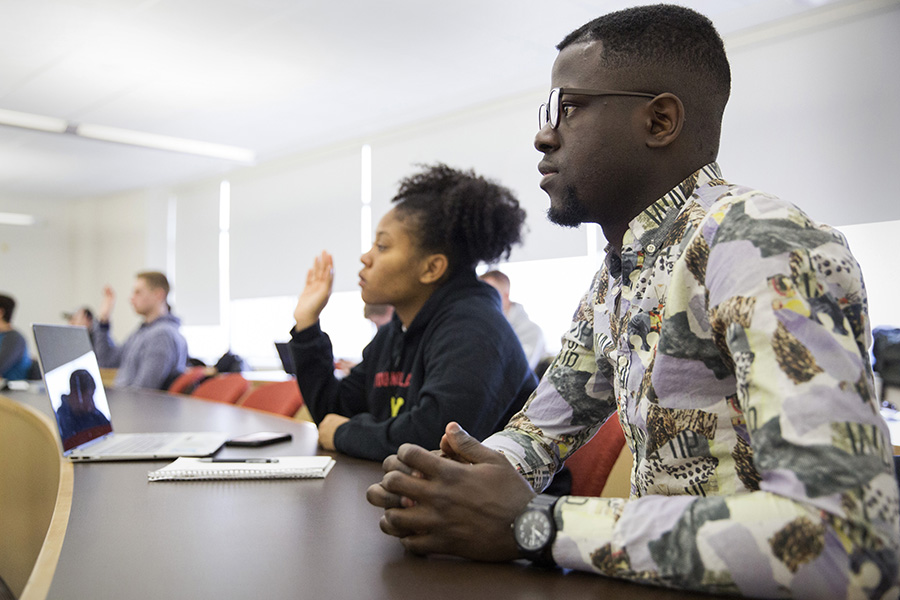 Students sit in a classroom and one student is raising their hand.