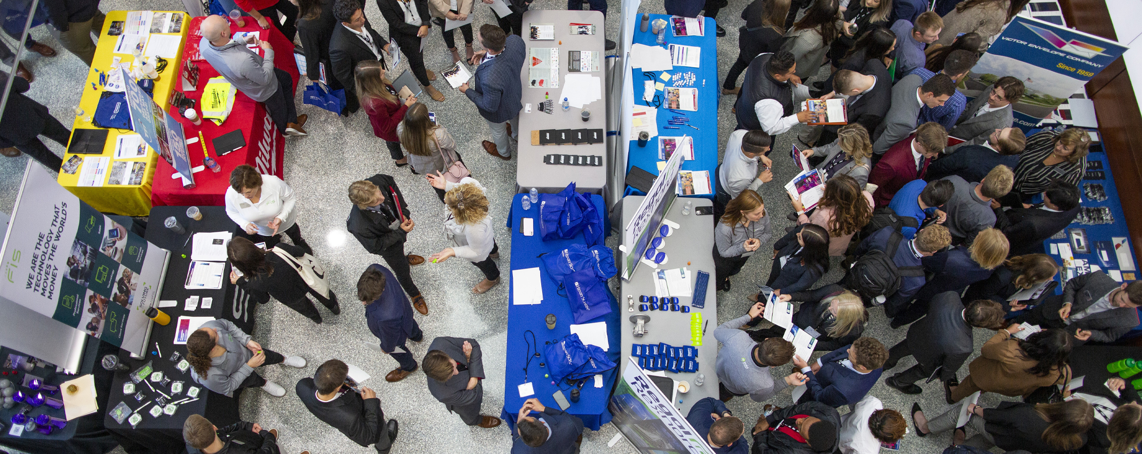 A photo from above shows people gathered at a conference banner signs in the aisles.