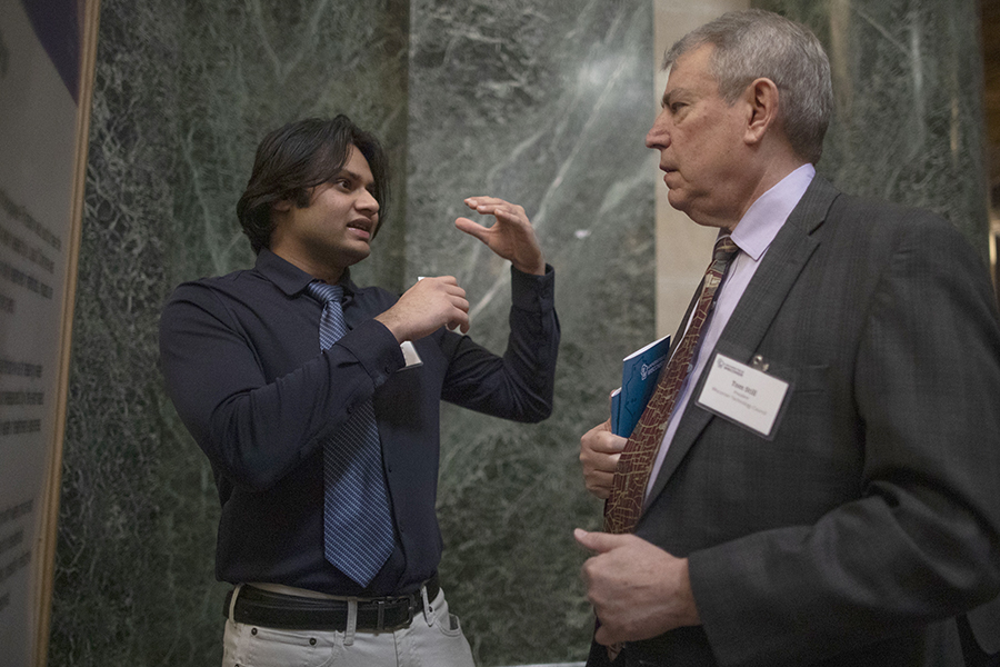 A business analytics student speaks to a senator in front of a green marble background.