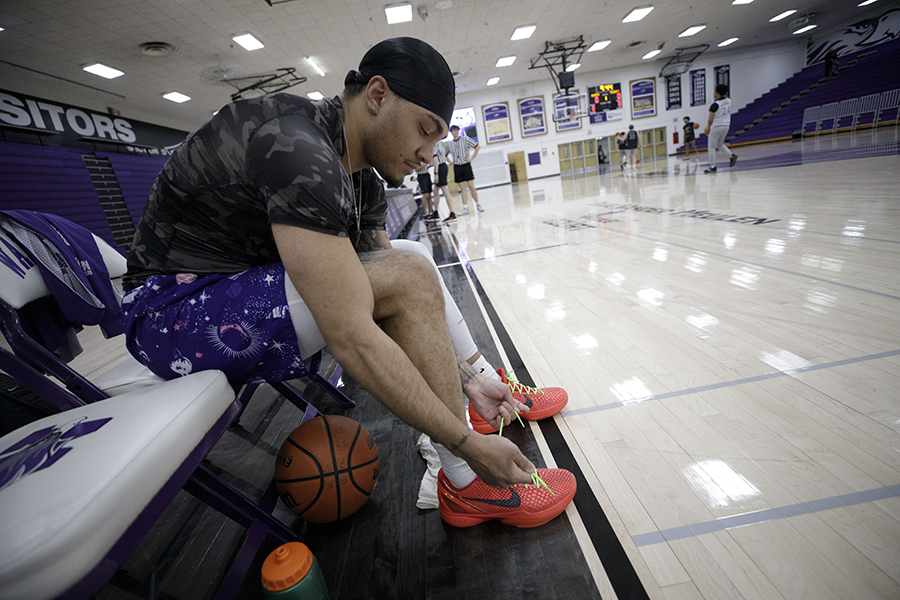 A student laces up their shoes in a basketball gym.