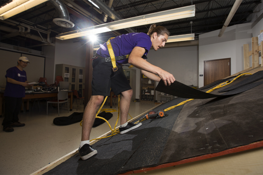 A student climbs on a mock roof during a roofing simulation.