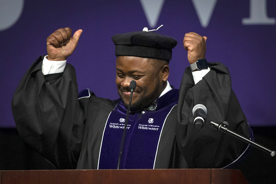 A person dressed in academic regalia smiles and throws their arms in the air at commencement.