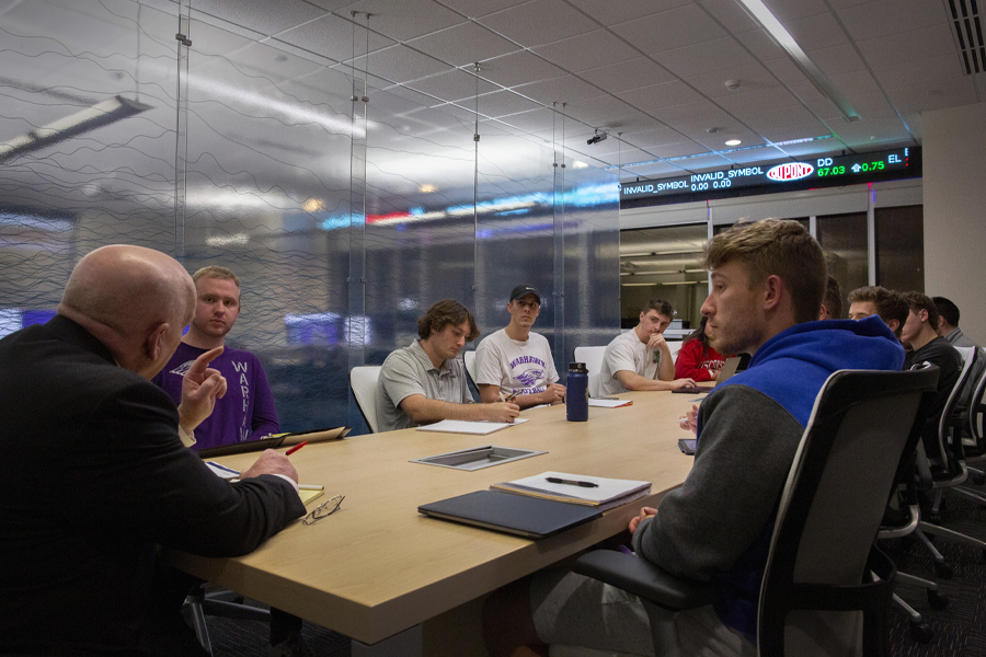 Students and a faculty member sit around a table with computer monitors in the background.