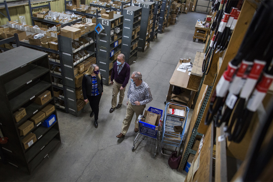 People walk through a warehouse with stacked boxes.