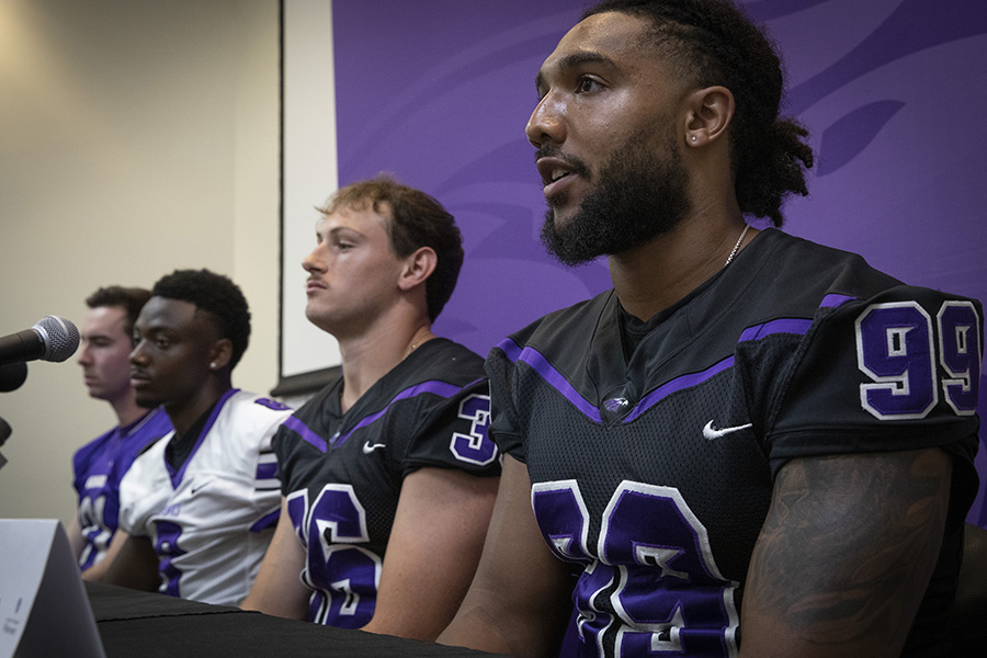 Warhawk football players wear their jerseys and sit together by a microphone during a press conference.