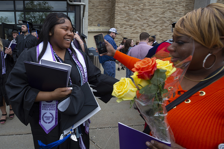 A student holds their diploma and smiles at graduation with their family.