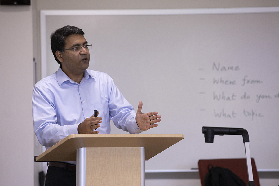 A faculty member teaches at the front of a classroom by a podium.