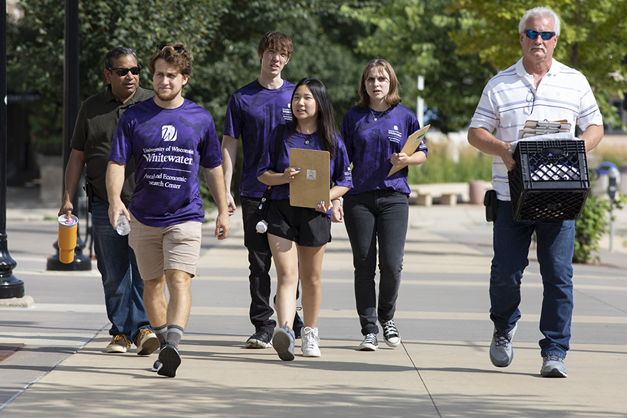 A group of students and a faculty member walk outdoors to collect information from people.