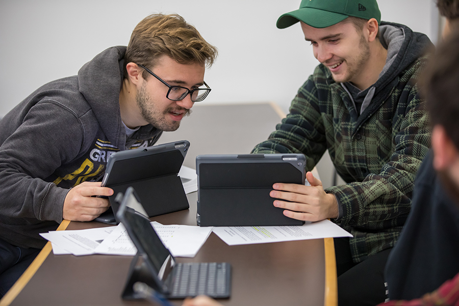 Two students work together on tablets in a classroom.