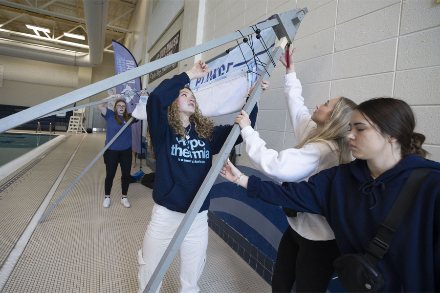 A group of students work together to put up a large sign on a pool deck.