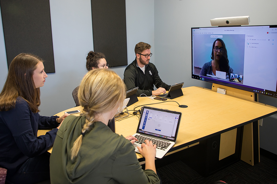 Students sit around a table and participate on a video call.