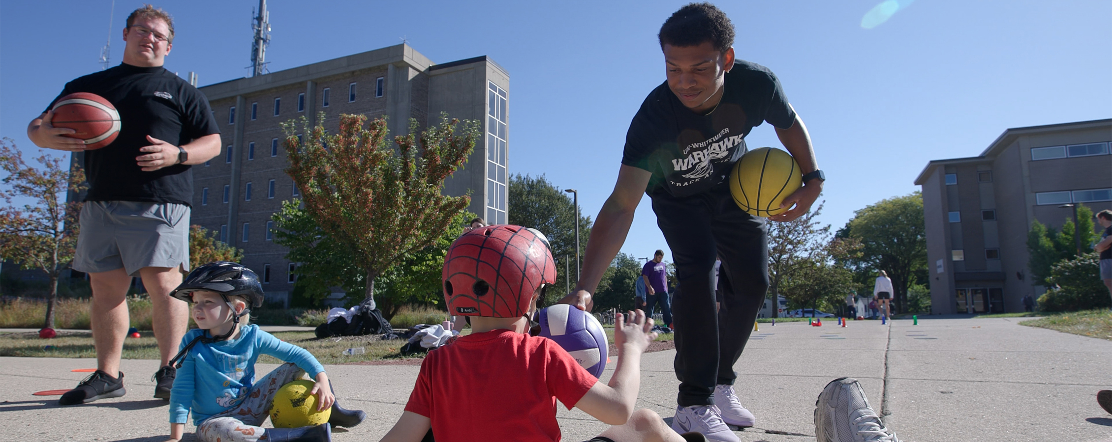 Two students and two children play with basketballs outdoors.