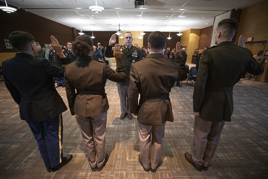 Four ROTC officers raise their hand as they take an oath in front of a military officer.
