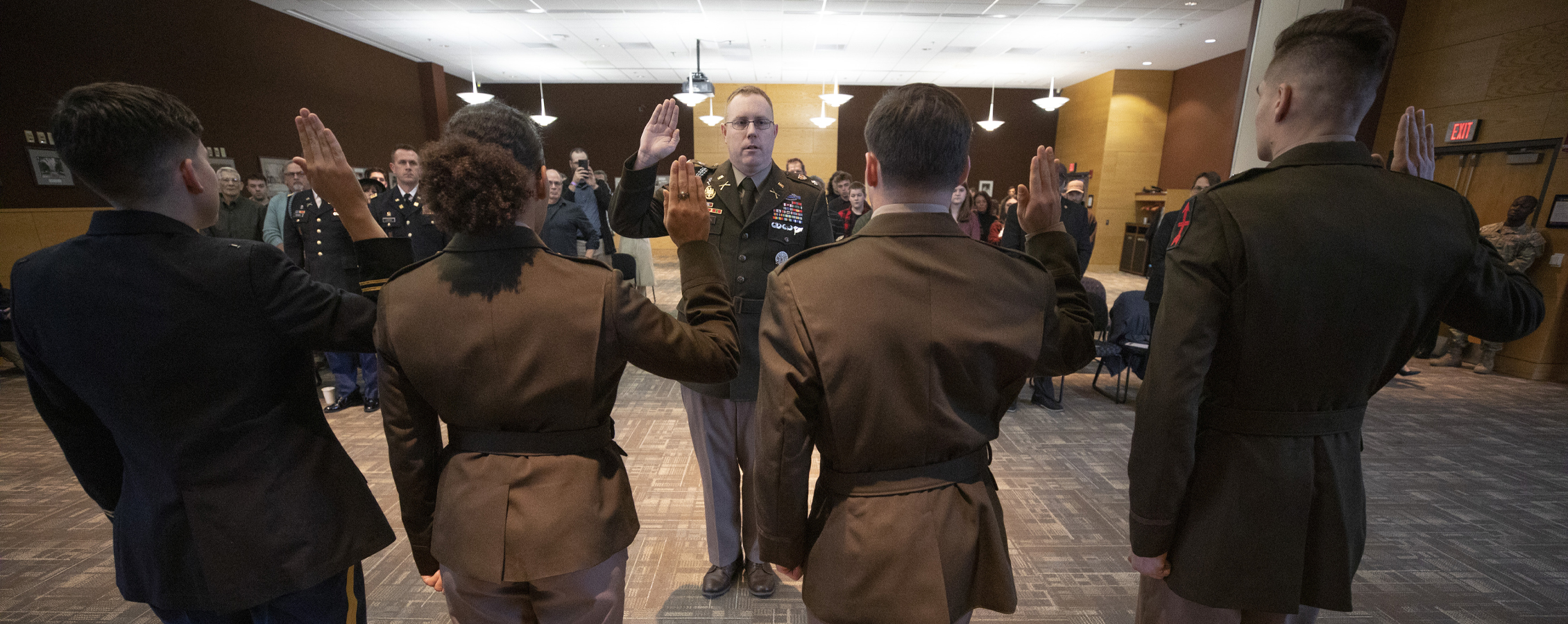 Four ROTC officers raise their hand as they take an oath in front of a military officer.