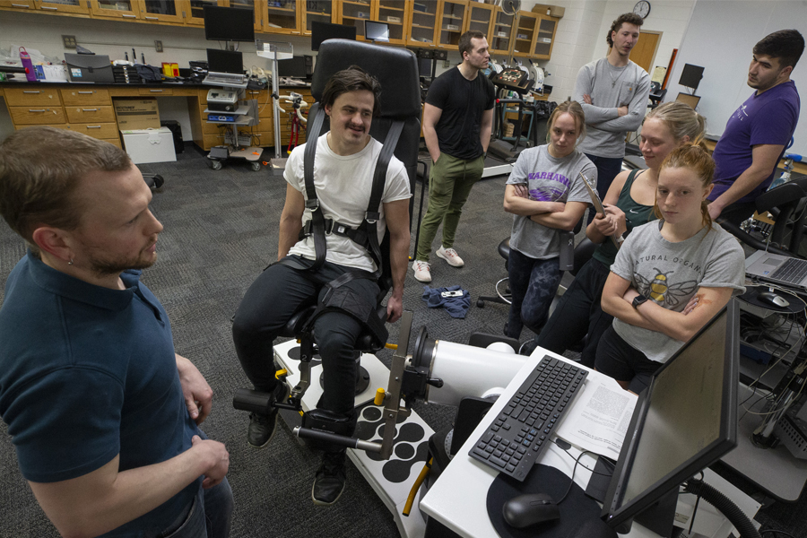 A faculty member and students gather around a student strapped in a chair to collect data during an exercise during class.