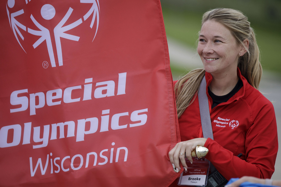 A person smiles and stands next to a red flag that says Special Olympics.