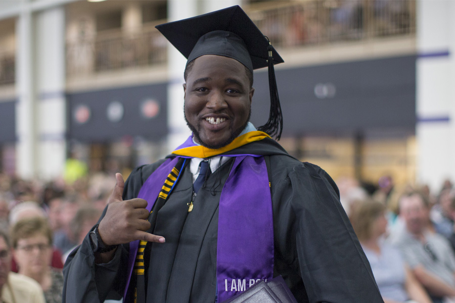 A person in academic regalia smiles at the camera during commencement.