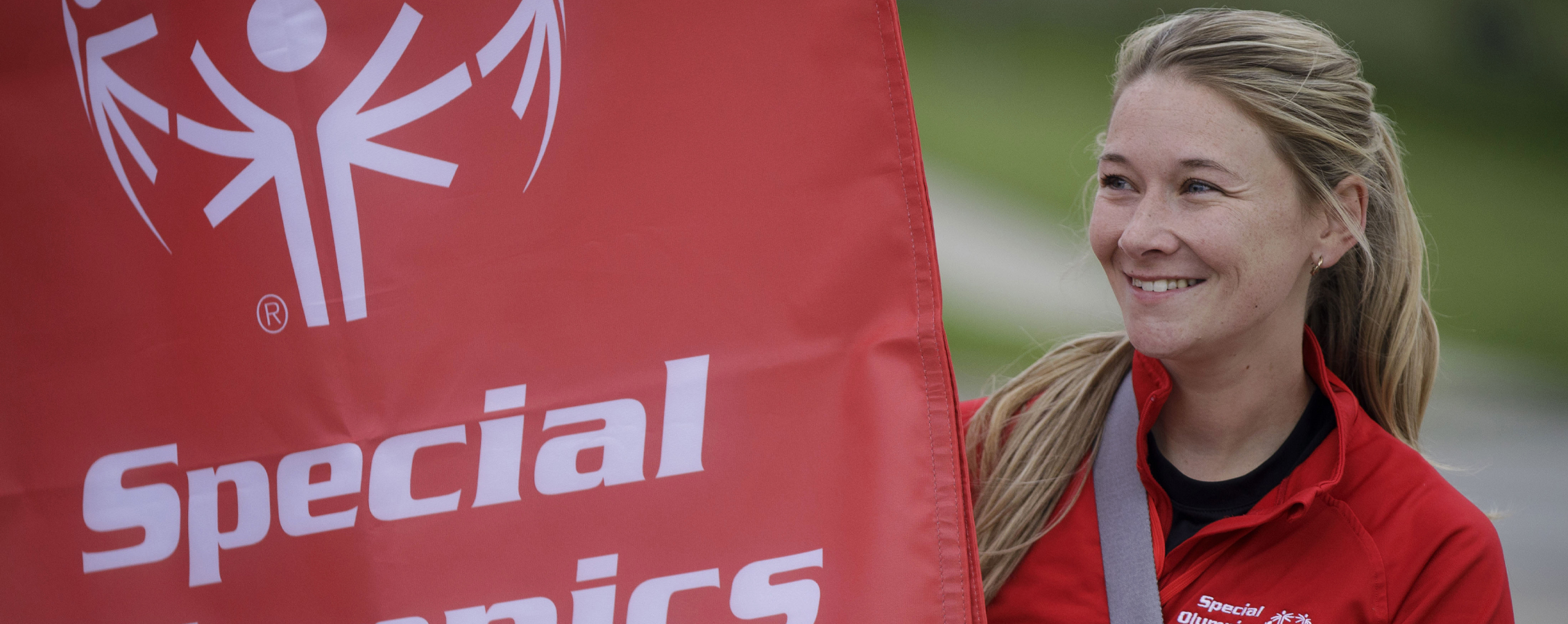 A person smiles and stands next to a red flag that says Special Olympics.