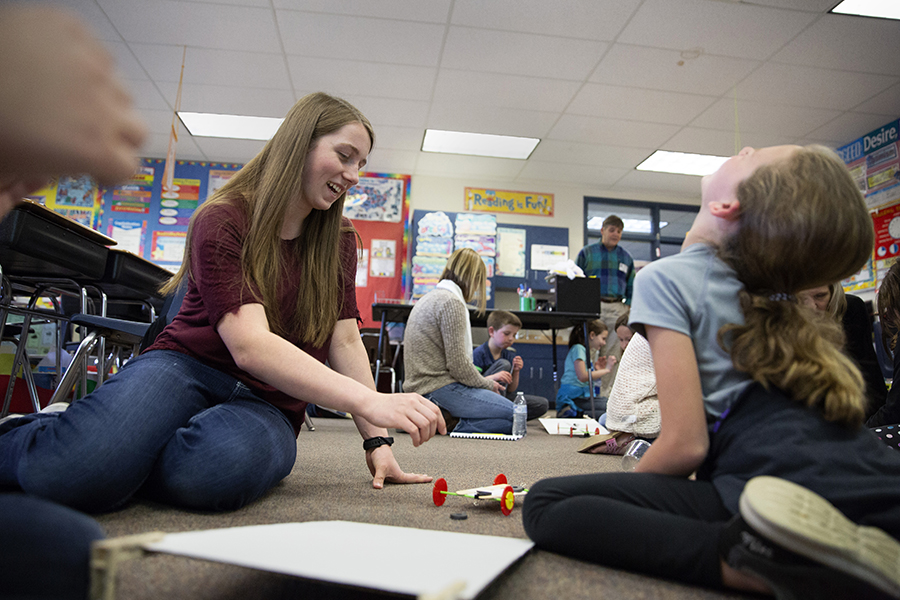 A young teacher sits on the ground with a child.