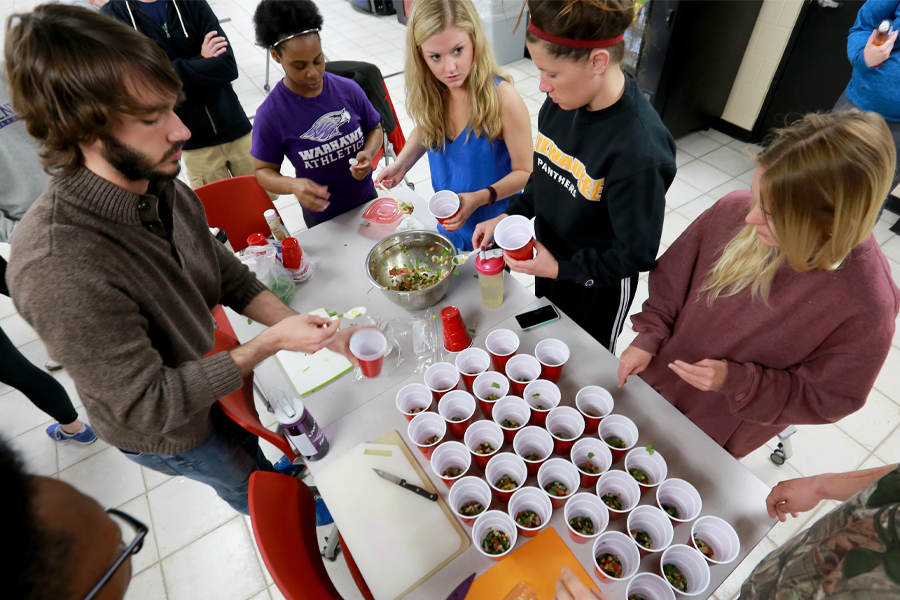 People gather around a table with red plastic cups filled with chopped food.