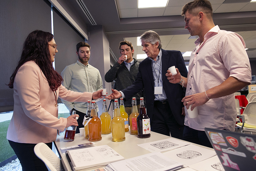 People gather around a table as a student hands out beverages.