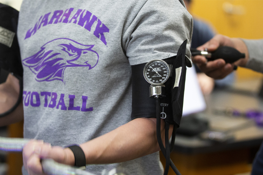 A pressure cuff is shown on the bicep of a person lifting a barbell.