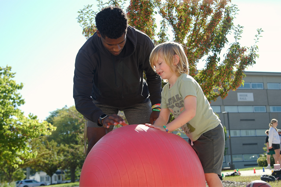 A student bounces a red ball with a child.