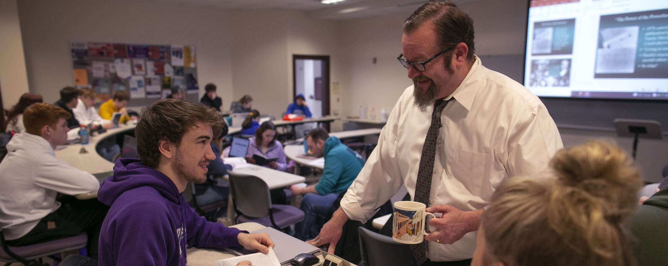 A professor visits with a student in class.