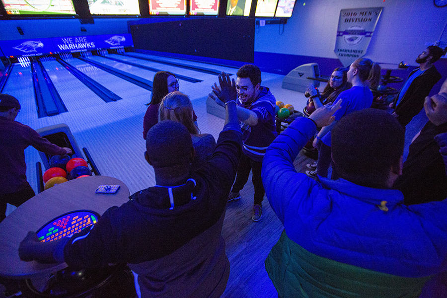 Student gather in the bowling alley with the black lights on.