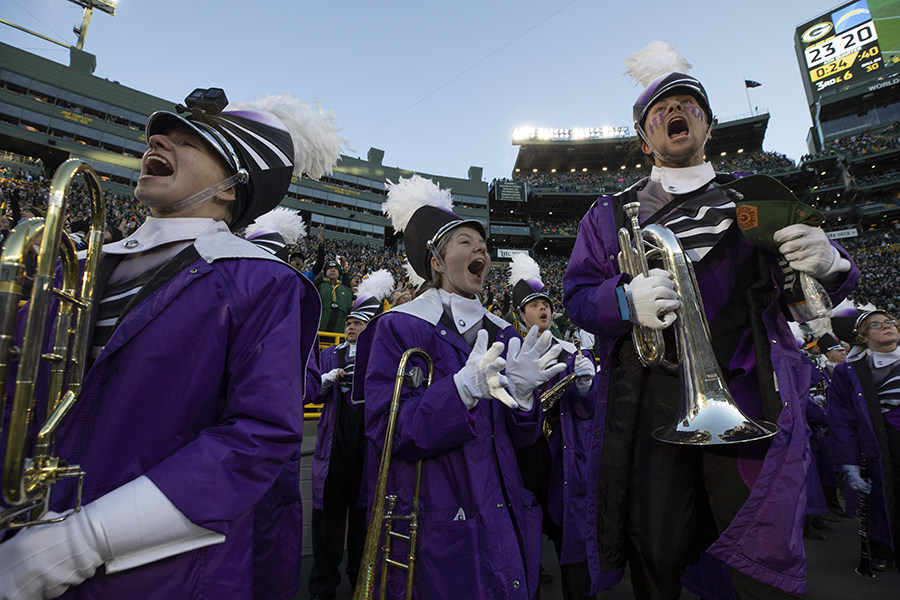 Students hold their instruments and yell with excitement while standing on the field at Lambeau Field.